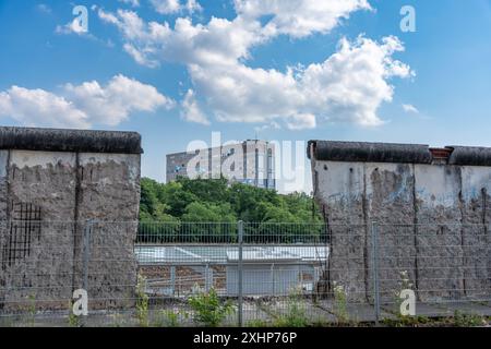 A house is visible in the breach of the old Berlin Wall. . The building is tall and has many windows. The sky is blue and there are clouds Stock Photo