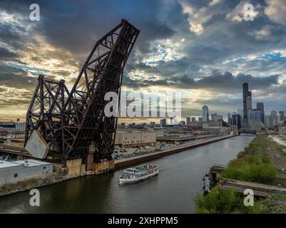 River boat passes under the St. Charles Air Line Bridge, steel railroad drawbridge over the Chicago river with dramatic sunset sky Stock Photo