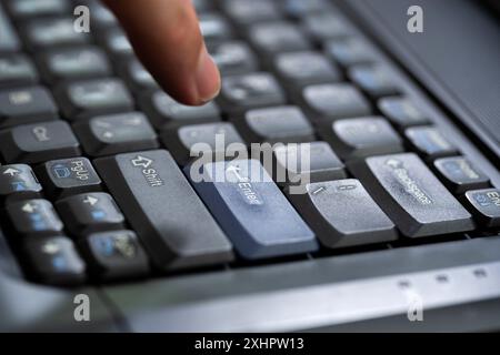 Mans finger about to press an enter key on a modern office laptop computer keyboard, hand hovering above the enter key, indecisive man ready to push t Stock Photo