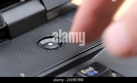 Man's finger reaching to press a generic laptop computer power button, about to turn the device on or off, hovering over the power key, object closeup Stock Photo