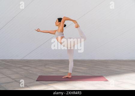 A bunette woman in sportswear doing the Natarajasana pose or dancer's pose with the background of modern buildings Stock Photo