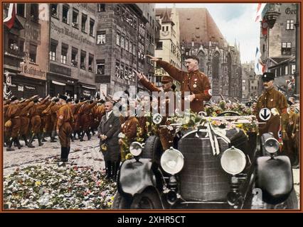 1927 Adolf Hitler standing in his open top Mercedes car at Nuremberg Rally Congress 1927 early colour postcard, with flowers thrown from admirers, giving his Nazi Heil Hitler salute to the parading & passing Sturmbteilung SA Troops in their brown shirt uniforms with swastika armbands. Julius Streicher a well known virulent anti semite and owner of Der Sturmer standing in front of Hitler in a dark suit. 1927 Stock Photo