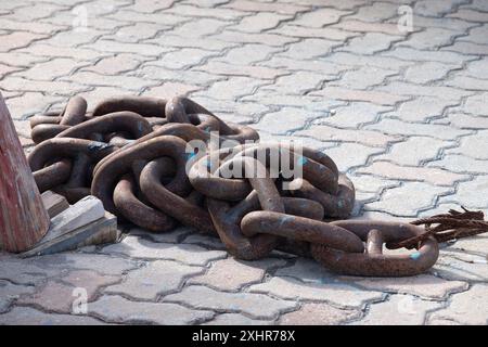 A chain of rusty metal links laying on a brick floor. The chain is broken and has a few pieces missing Stock Photo