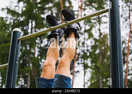 A mans legs in gravity boots hangs on a horizontal bar outdoors on a summer day. Stock Photo