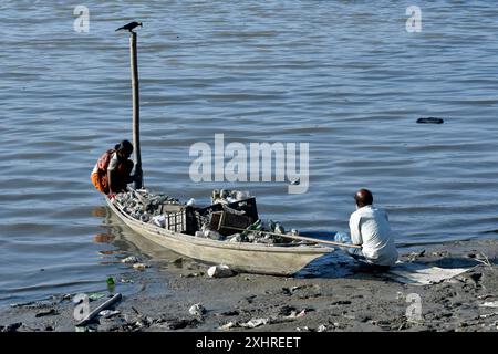 Man and women rag picker collecting plastic bottle and other plastic materials in a boat from the bank of Brahmaputra River in Guwahati, Assam, India Stock Photo