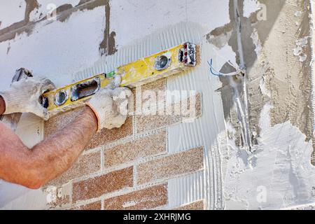 House painter uses spirit level to ensure faux brick panel is accurately positioned relative to horizontal plane. Stock Photo