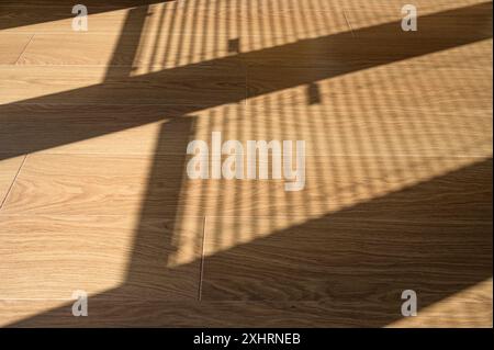 Sunlight and shadows of window blinds falling on to a wooden floor in the morning Stock Photo