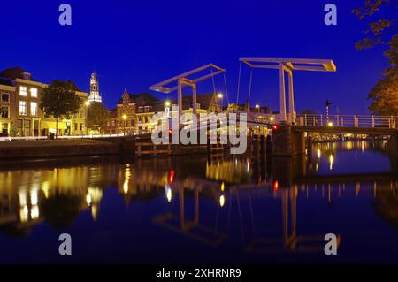 An illuminated canal with bridge and historic buildings in the background at night, evening mood, Haarlem, Netherlands Stock Photo