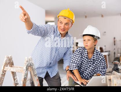 Man architect and boy using laptop while discussing working process in house being renovated Stock Photo