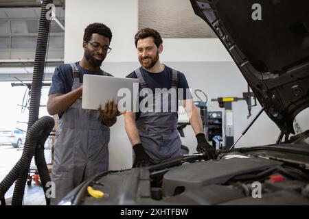 Two mechanics diagnosing car issue with laptop in garage Stock Photo