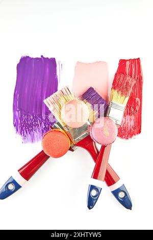 Three paintbrushes with red handles, each dipped in colorful paint, with matching macarons on a white background. Stock Photo