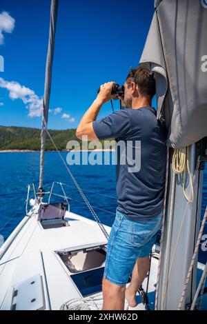 Young man captain on the yacht looking through binoculars during sailing boat. Travel and active life. Yachting Stock Photo