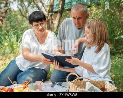 Family spending time together on a picnic.  Grandparents and granddaughters reading a book on a summer picnic Stock Photo