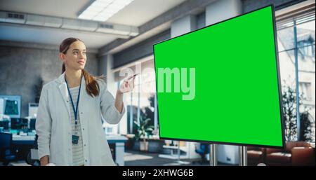 Excited Young Female Specialist Doing a Presentation, Using Green Screen Monitor and Talking to her Colleagues in a Laboratory. Team of Engineers Having a Meeting, Brainstorming While Using Technology Stock Photo