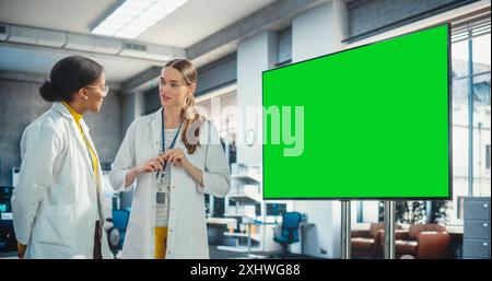 Excited Young Female Specialist Doing a Presentation to her Colleague And Using Green Screen Chromakey Television Set in a Laboratory. Professional Engineer Pitching Manufacturing Ideas to Team Lead. Stock Photo