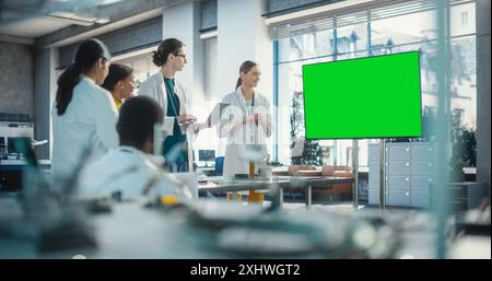 Group of Students Listening to Their Robotics Female Professor Who Uses Green Screen Monitor in a Laboratory. Team of Engineers Having Meeting and Discussing Manufacturing Ideas, Using Technology Stock Photo