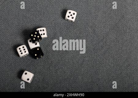 White dice with black markings. They lie on a surface covered with a coarse gray cloth. Among them are two black dice with white markings. Stock Photo