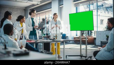 Group of Students Listening to Their Robotics Female Professor Who Uses Green Screen Monitor in a Laboratory. Team of Engineers Having Meeting, Discussing Manufacturing Ideas, Using High Technology Stock Photo