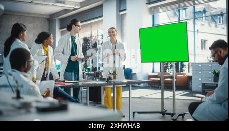 Group of Students Listening to Their Robotics Female Professor Who Uses Green Screen Monitor in a Laboratory. Team of Engineers Having Meeting and Discussing Manufacturing Ideas, Using High Technology Stock Photo