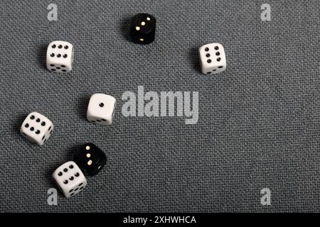 White dice with black markings. They lie on a surface covered with a coarse gray cloth. Among them are two black dice with white markings. Stock Photo