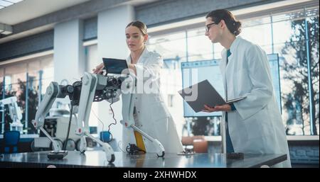 Male Project Manager and Female Machinery Operator Collaborate on a Mobile Robot Animal Project, Using Laptop Computer. Two Professional Engineers Brainstorming, Discussing Futuristic AI Pet Stock Photo