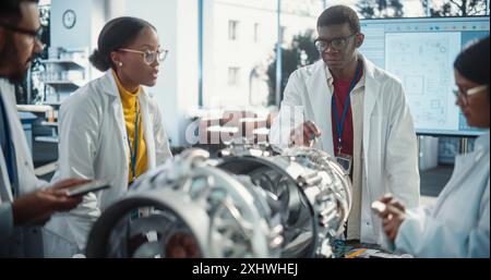 Young Black Engineer Instructing and Leading his Team, Analyzing and Researching How a Futuristic Turbofan Motor Works. Diverse Scientists Developing Innovative Technology in Industrial Facility Stock Photo