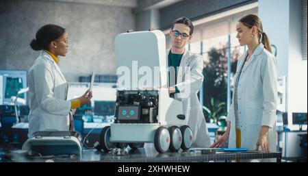 Team of Industrial Specialists Working on Mobile Robot, Using Laptop. Young Male and Female Engineers in a Lab Discussing an Automated AI Robotic Delivery Assistant, Brainstorming Improvement Ideas Stock Photo