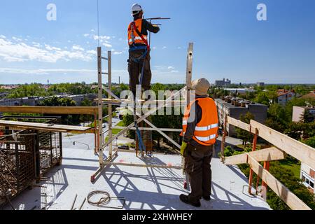 Supervisor, foreman look out on worker tying armature to make a reinforcing frame for concrete pillar, he carry fall arrestor device, hooks for safety Stock Photo