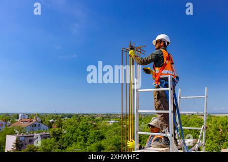 Two workers are using tape measure to measure dimensions, armature length of reinforcing frame for concrete pillar, he carry fall arrestor device, hoo Stock Photo