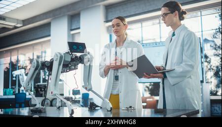 Male Project Manager and Female Machinery Operator Collaborate on a Mobile Robot Animal Project, Using Laptop Computer. Professional Engineers Brainstorming, Discussing Futuristic AI Pet Stock Photo