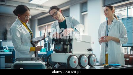 Diverse Team of Industrial Specialists Working on Remotely Controlled Robot, Using Laptop. Young Male and Female Engineers Discussing an Autonomous AI Delivery Assistant Prototype, Brainstorming Stock Photo