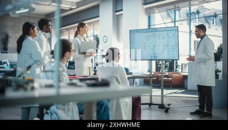 Diverse Team of Males and Females Discussing Ideas in Technological Modern Startup Lab. Group of International Students Listening to Their Robotics Professor While He Explains AI Robot Blueprints Stock Photo