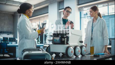 Diverse Team of Industrial Specialists Working on Remotely Controlled Robot, Using a Laptop. Young Male and Female Engineers Discussing an Autonomous AI Delivery Assistant Prototype, Brainstorming Stock Photo