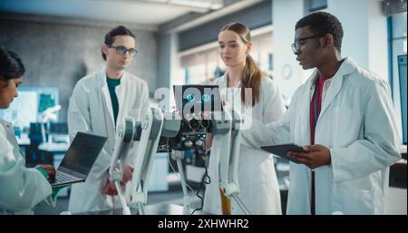 Diverse Team of Industrial Robotics Specialists Gathered Around a Table With Mobile Robot. Engineers In Lab Coats Discussing an Automated AI Robotic Dog, Using Laptop and Tablet and Brainstorming. Stock Photo
