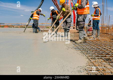 Team of construction workers are pouring and leveling fresh concrete using handmade tool over rectangular armature. Stock Photo