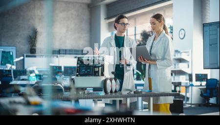 Two Industrial Robotics Specialists Working on a Mobile Robot, Using Laptop. Young Male Engineer In Lab Coat Discussing an Automated AI Robotic Delivery Assistant with his Female Project Supervisor Stock Photo
