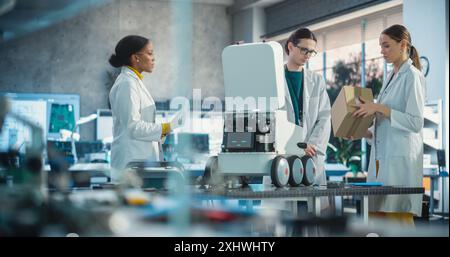 Team of Industrial Specialists Working on Mobile Robot, Using a Laptop. Young Male and Female Engineers in a Lab Discussing an Automated AI Robotic Delivery Assistant, Brainstorming Improvement Ideas Stock Photo