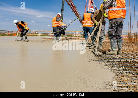 Team of construction workers are pouring and leveling fresh concrete using handmade tool over rectangular armature. Stock Photo