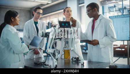 Diverse Team of Industrial Robotics Specialists Gathered Around a Table With a Mobile Robot. Engineers In Lab Coats Discussing an Automated AI Robotic Dog, Using Laptop and Tablet Computer. Stock Photo