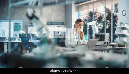 Portrait of Professional Female Scientist Working in Industrial Lab Using Laptop Computer. Successful Engineer Checking and Monitoring Production Quality, Analysing Data Using Advanced Technology Stock Photo