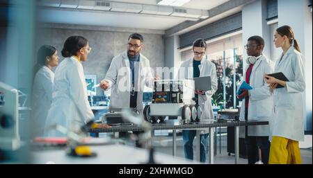 Diverse Team of Industrial Robotics Specialists Gathered Around a Table With a Mobile Robot. Engineers In Lab Coats Discussing an Automated AI Robotic Delivery Assistant, Using Laptop, Tablet Computer Stock Photo