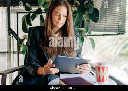 A young businesswoman sitting at a table in a coffee shop uses a digital tablet to work. Stock Photo