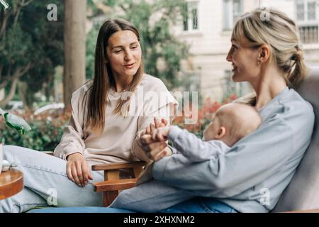 Two women talk about motherhood while nursing a baby while sitting in a cafe. Stock Photo