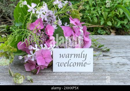 Greeting card with pink hydrangeas, soapwort, oregano and text: warmly welcome Stock Photo