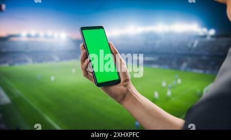 Sport Stadium Championship: Person's Hand Holding Green-Screen Chroma Key Smartphone. Great Sports Related Copyspace Template Connected to Social Media, Checking Score, Results. Stock Photo