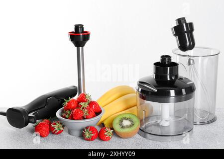 Hand blender kit, fresh fruits and strawberries on gray table against white background Stock Photo