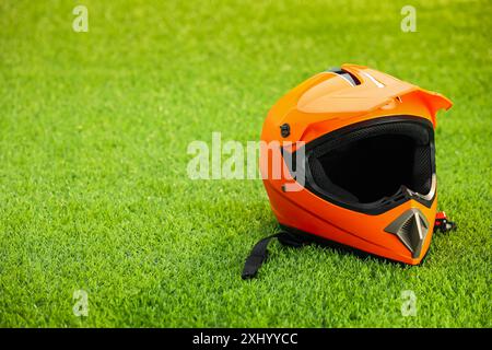 Orange motorcycle helmet with visor on green grass, space for text Stock Photo