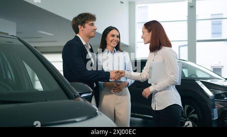 Caucasian couple clients buyers conclude agreement deal buy buying new car auto automobile in showroom rental service rent transport shaking hands Stock Photo