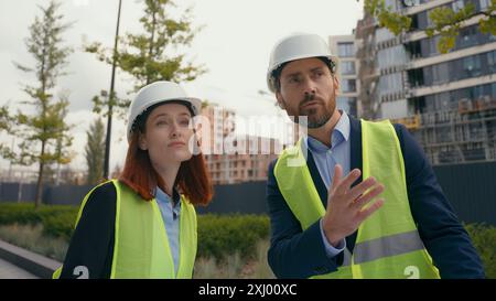 Contractors diversity engineers two people colleagues man woman builders architects wearing safety uniform protective helmets hardhats talking looking Stock Photo