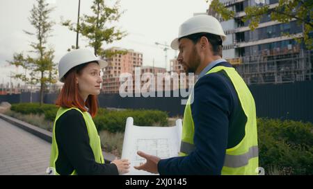 Two contractors civil engineers checking information in blueprint discuss teamwork pointing city buildings project managers planning collaboration Stock Photo